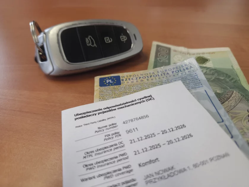 Dokument polisy ubezpieczenia OC na 2026 rok leżący na blacie obok dowodu rejestracyjnego, kluczyka samochodowego i banknotu - obrazujące rosnące kary z UFG za brak ważnego ubezpieczenia