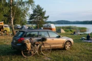 Rower turystyczny oparty o samochód na kempingu nad jeziorem w letni wieczór, w tle namioty i przyczepy kempingowe