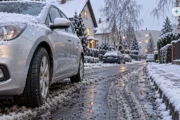 Obraz wygenerowany przez AI. Przednie koło samochodu z letnią oponą w błocie pośniegowym na osiedlowej ulicy po pierwszym śniegu, opony letnie zimą a ubezpieczenie OC i AC
