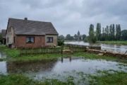 Dom jednorodzinny nad rozlaną rzeką i worki z piaskiem przy ogrodzeniu, ubezpieczenie domu od powodzi
